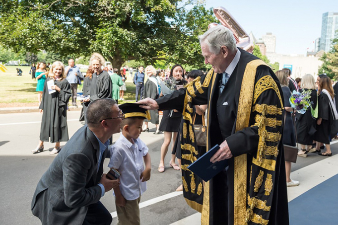 U of T Chancellor Michael Wilson lets a young boy try on his ceremonial hat at the June 2018 Convocation. Photo by Steve Frost.