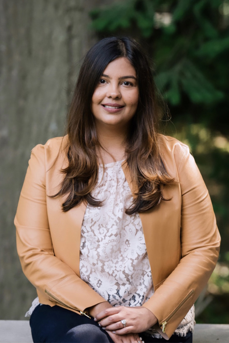 Sabina Vohra-Miller smiles gently as she sits outside under a tree