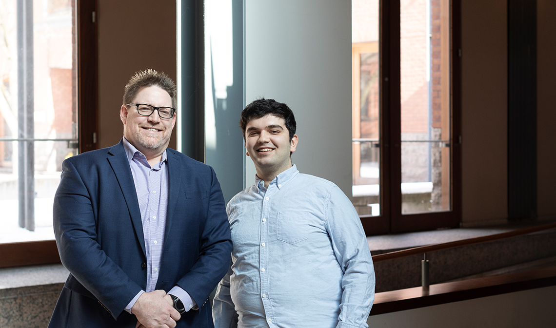 Jeff Beleskey on the left and Ali Aghaeinia on the right, standing and smiling inside Woodsworth College.