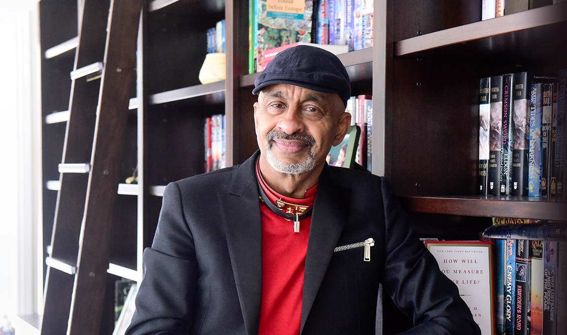 Ravi Gukathasan smiles in front of a bookshelf.