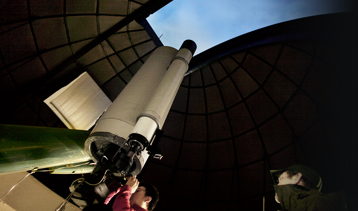 A person looking into a telescope through observatory ceiling.