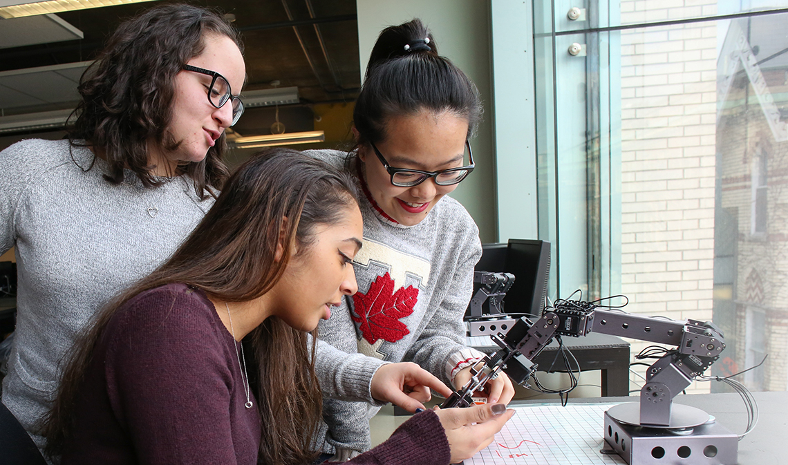 Three students focusing on small robotic arm.
