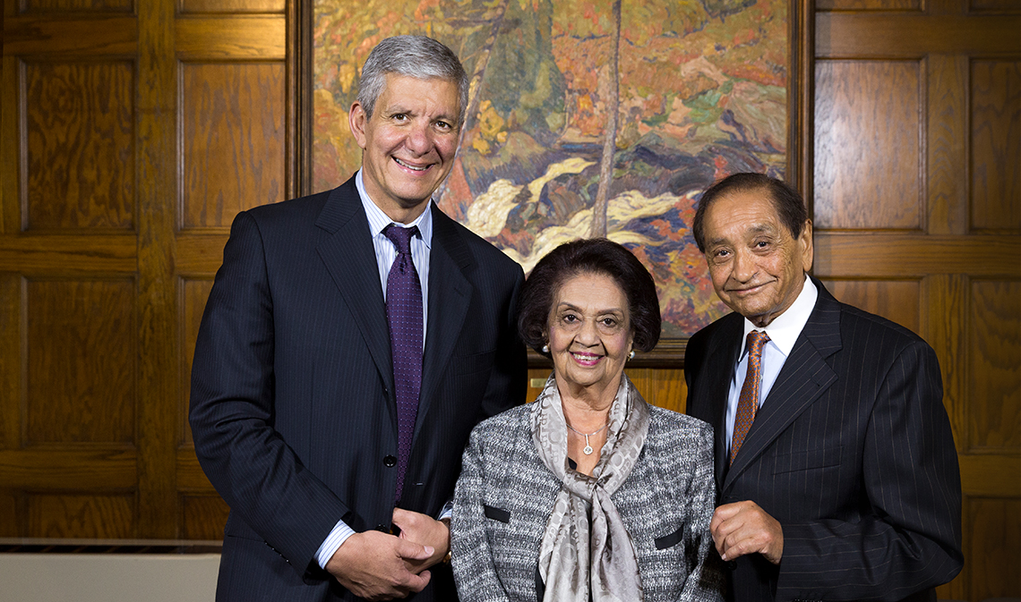 Sherif El-Defrawy, Gulshan Nanji and Pyarali Nanji standing and smiling in front of a wood panel wall with a painting in the background.