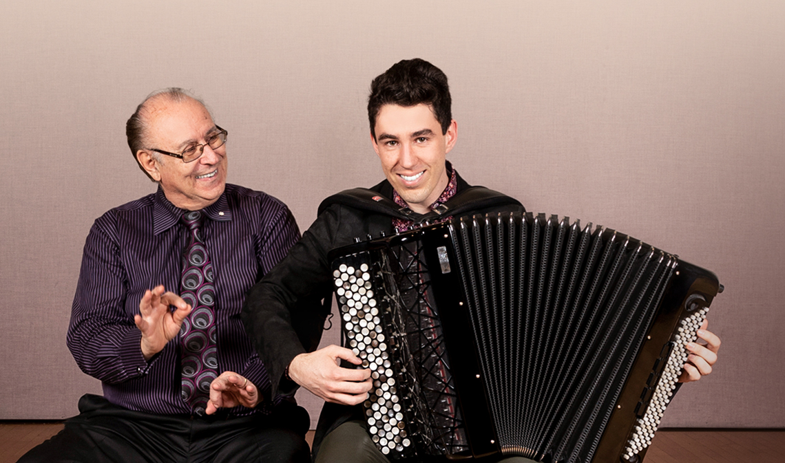 Joseph Macerollo (left) and Michael Bridge sitting and smiling, while Michael plays the accordion.