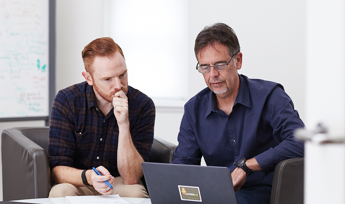 Ronald Deibert (right), seated with a student as they both look at an open laptop.