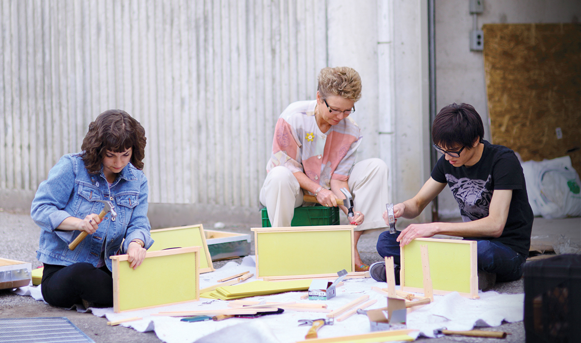 Three people assembling bee-hive panels outside.